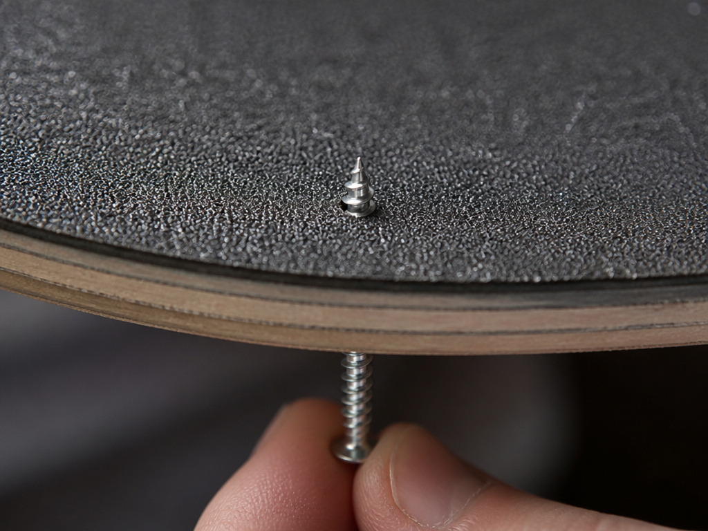 Close-up of puncturing grip tape for truck holes from underneath a skateboard.